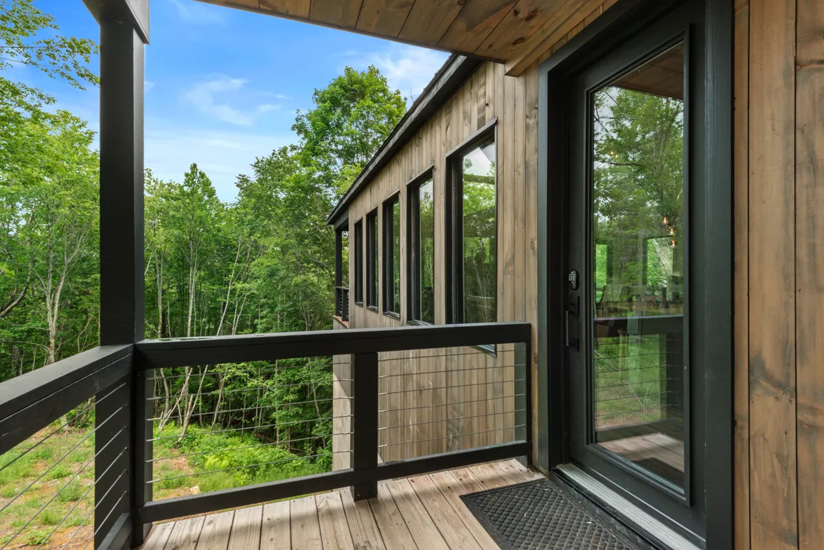 A peaceful balcony scene with a wooden railing, expansive windows reflecting greenery, and forested surroundings. It suggests spaces for taking in the view, fresh air, and connecting with nature—right outside the retreat.