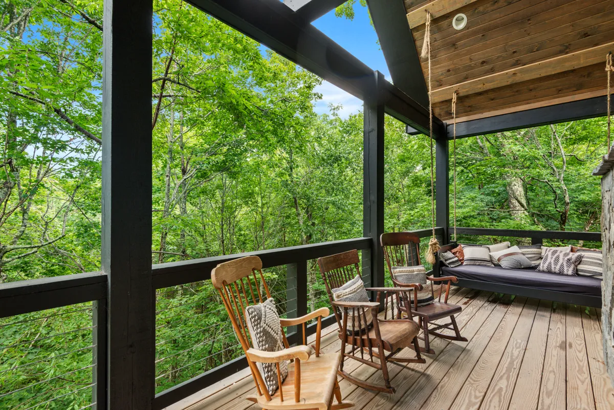 A cozy exterior porch scene with classic rocking chairs, a swing bed, and surrounding lush greenery. The outdoor space offers privacy and comfort, inviting guests to relax, read, or take breaks between work sessions.