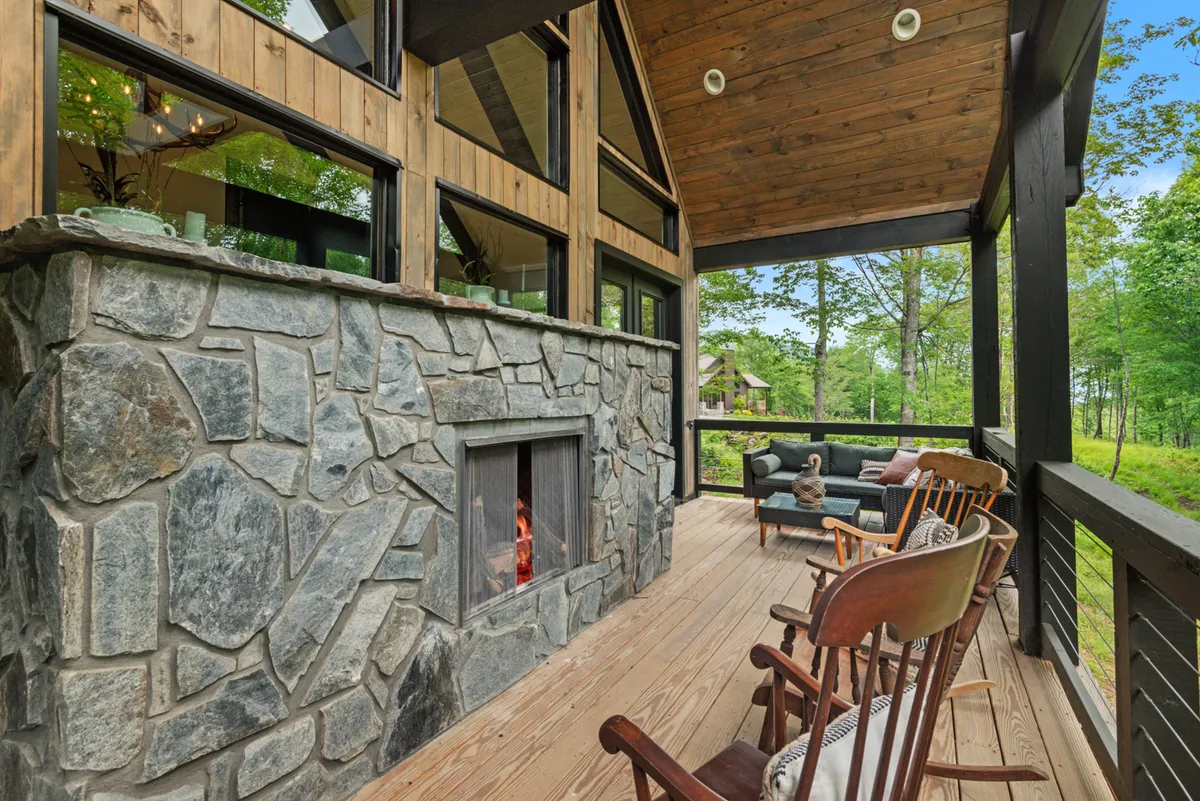 A cozy exterior deck with a stone fireplace, rocking chairs, and large windows. The inviting setup suggests relaxing moments after a day outdoors, while still enjoying views and the fresh mountain air.