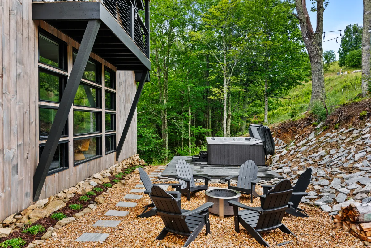 The image features a hot tub and a fire pit with Adirondack chairs arranged for socializing, set against a wooded backdrop. The area evokes communal gatherings under the stars, and the dual presence of the fire pit and hot tub echoes the section's themes of relaxation and togetherness.
