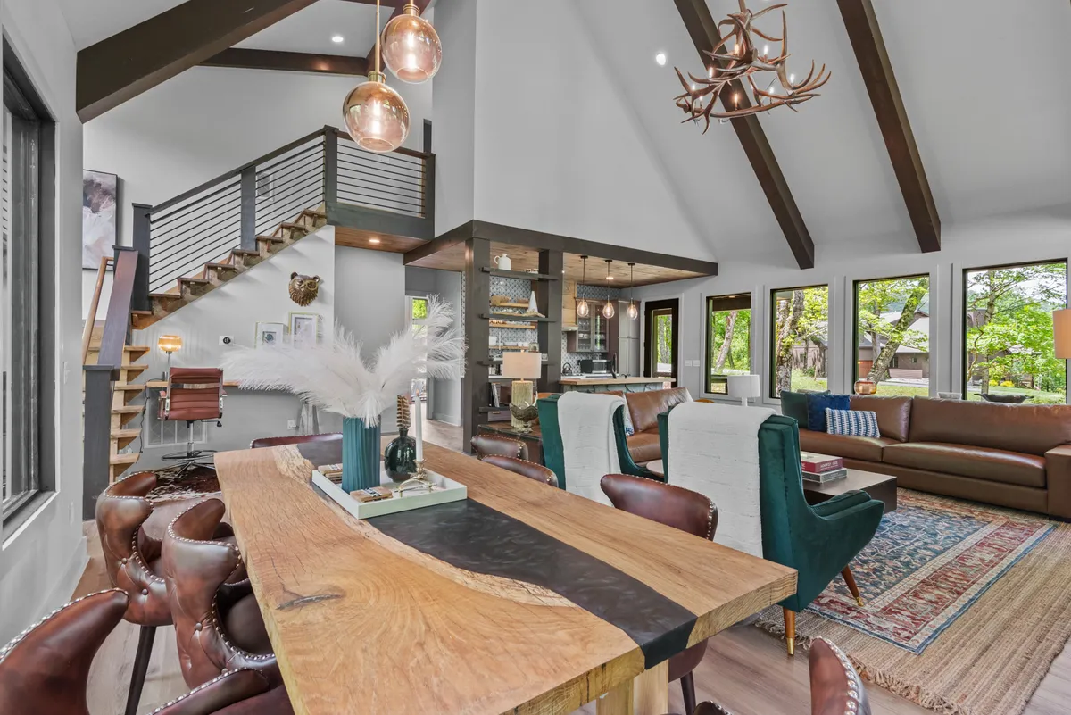 A beautifully arranged interior shot centered on a large wooden dining table, stylish bar stools at a kitchen island, and a spacious living area with a comfortable sofa. The kitchen features modern appliances and sleek cabinetry, while an abundance of natural light pours in through expansive windows. The overall mood is warm, inviting, and perfectly suited for both entertaining and relaxing family gatherings.