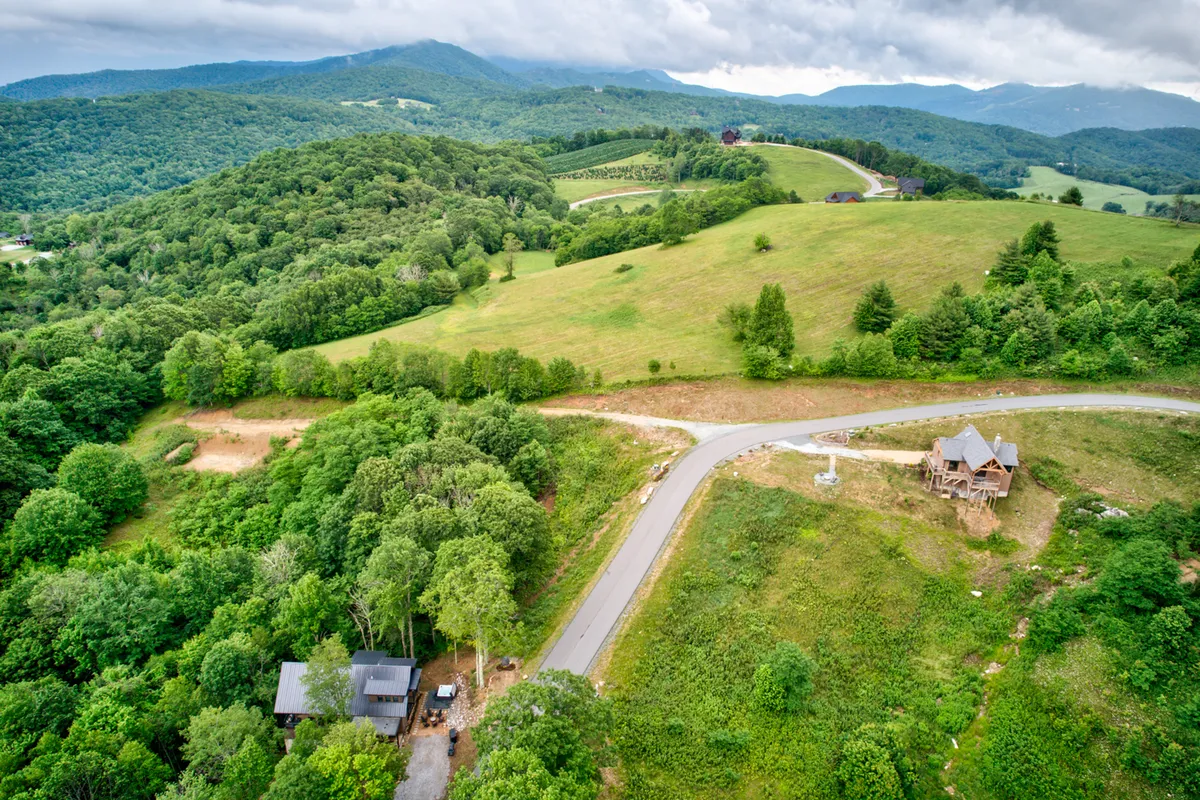 A tranquil scene featuring a new construction home nestled among rolling hills and dense greenery. A scenic road winds past the property, highlighting immediate access to local outdoor experiences and the home’s fresh, modern appeal.